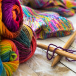 Colorful skeins of wool with knitting needles and sweater on woo | ASD Market Week arts, crafts hobby trade show