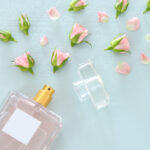 Top view image of perfume bottle with rose petals flowers over pastel blue background. Floral scent concept. | ASD Market Week